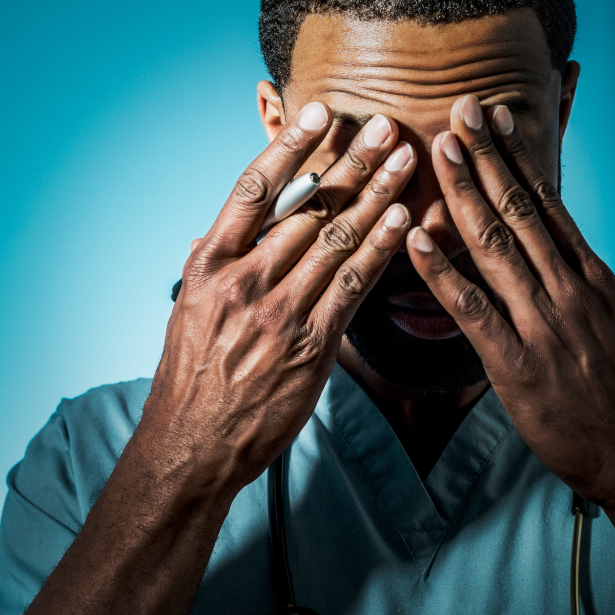 An exhausted male doctor rubs his eyes.